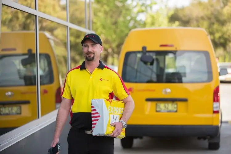 Man walking in front of a building and yellow van holding a package